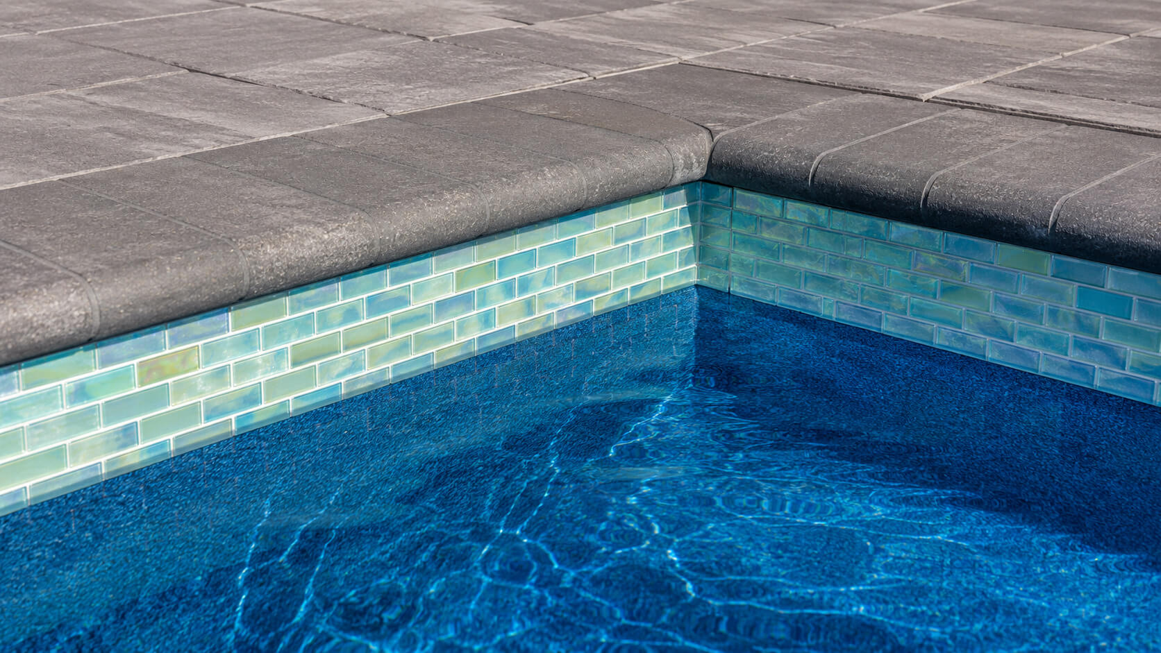 Gray paver pool coping above an iridescent turquoise glass waterline tile