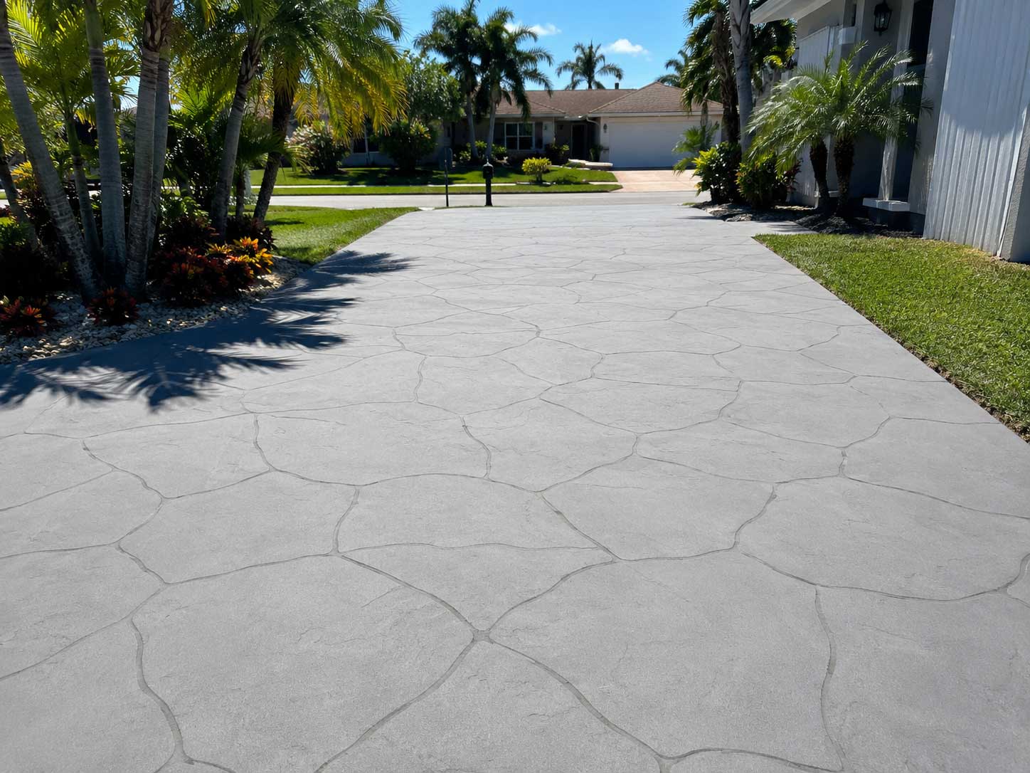 Gray stamped concrete driveway with a natural flagstone pattern and tropical landscaping