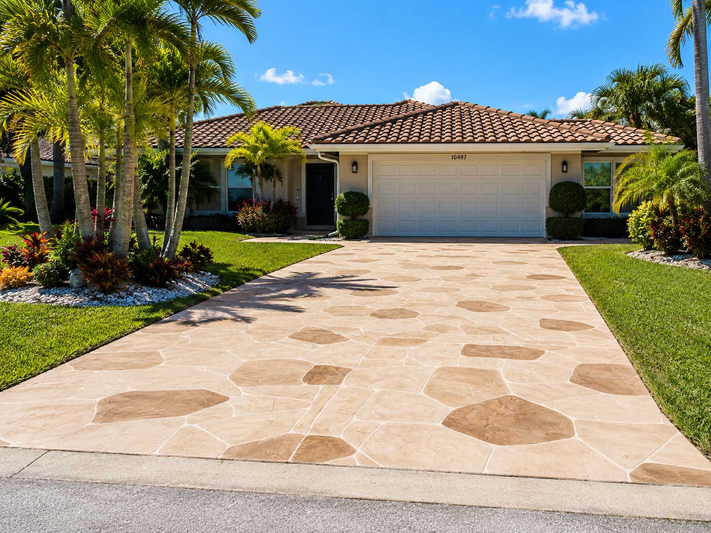 Tan decorative concrete driveway with contrasting stone shapes in front of a tropical home
