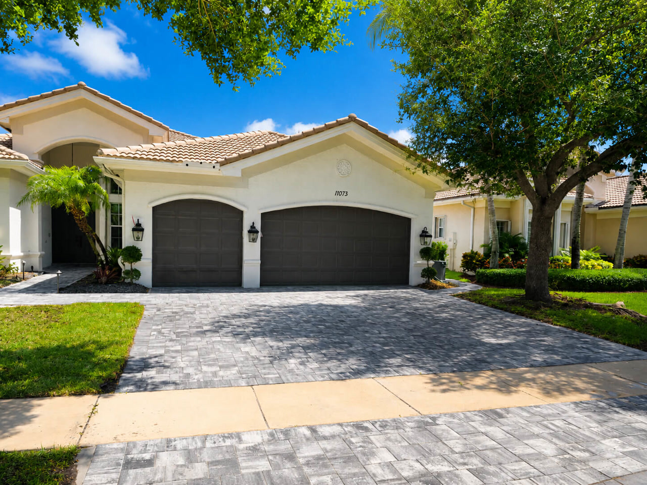 Finished gray paver driveway spanning a three car garage at a Mediterranean style home along a Juno Beach driveway