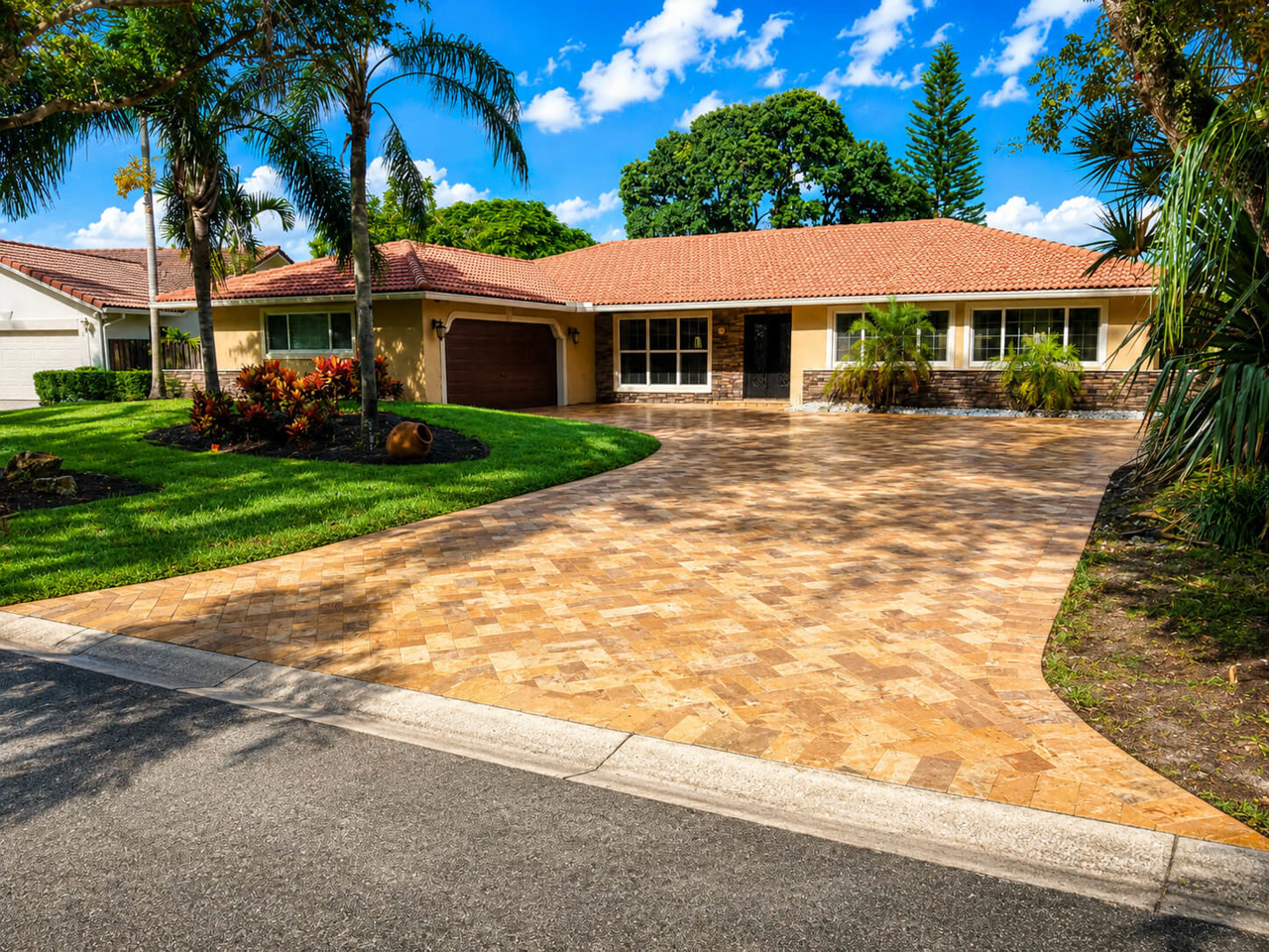 Wide herringbone travertine driveway curving up to a terracotta tile roof home for a Jupiter homeowner