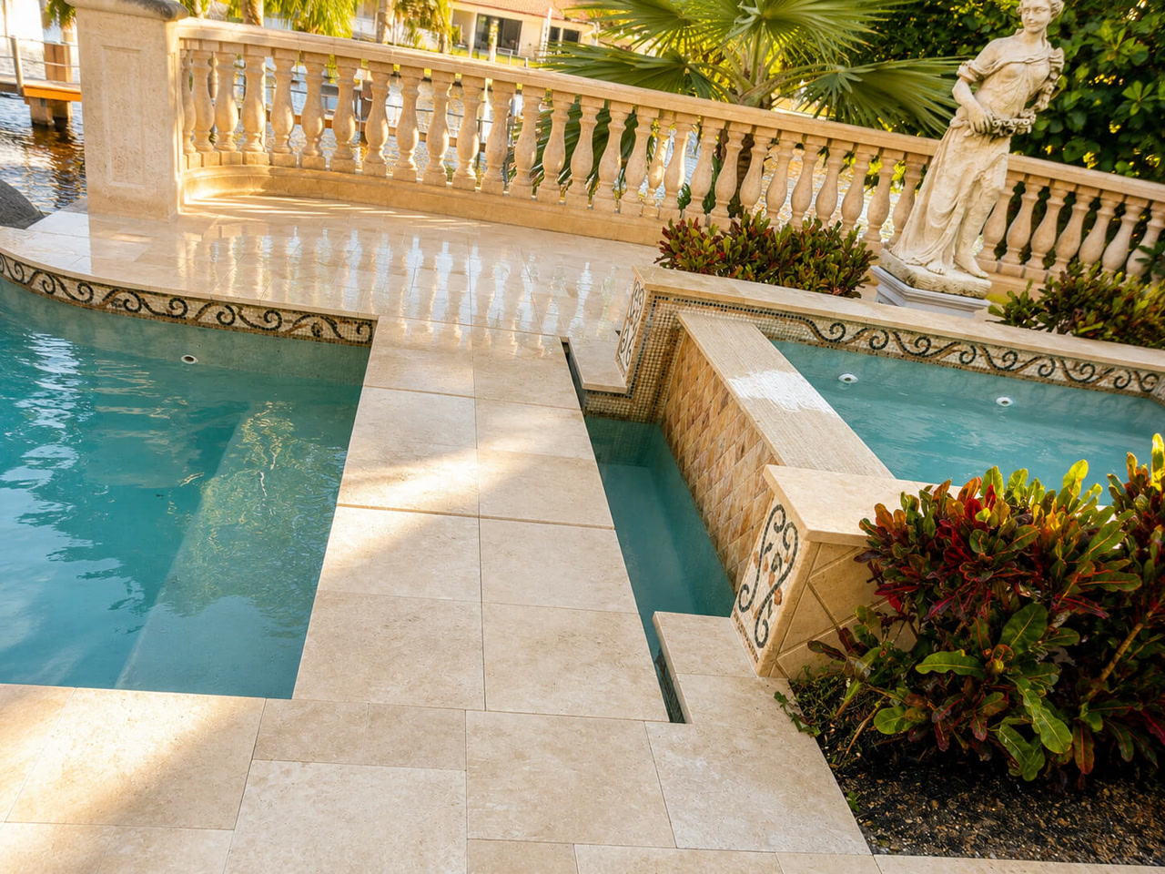 Ivory paver pool deck with a stone balustrade and mosaic tile spillway at a Pompano Beach waterfront estate