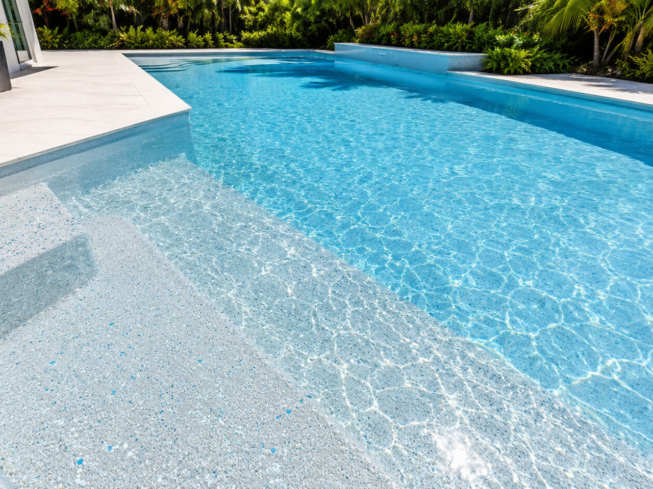 Light pebble pool finish under clear water across wide entry steps and a sun shelf at a Pompano Beach residence