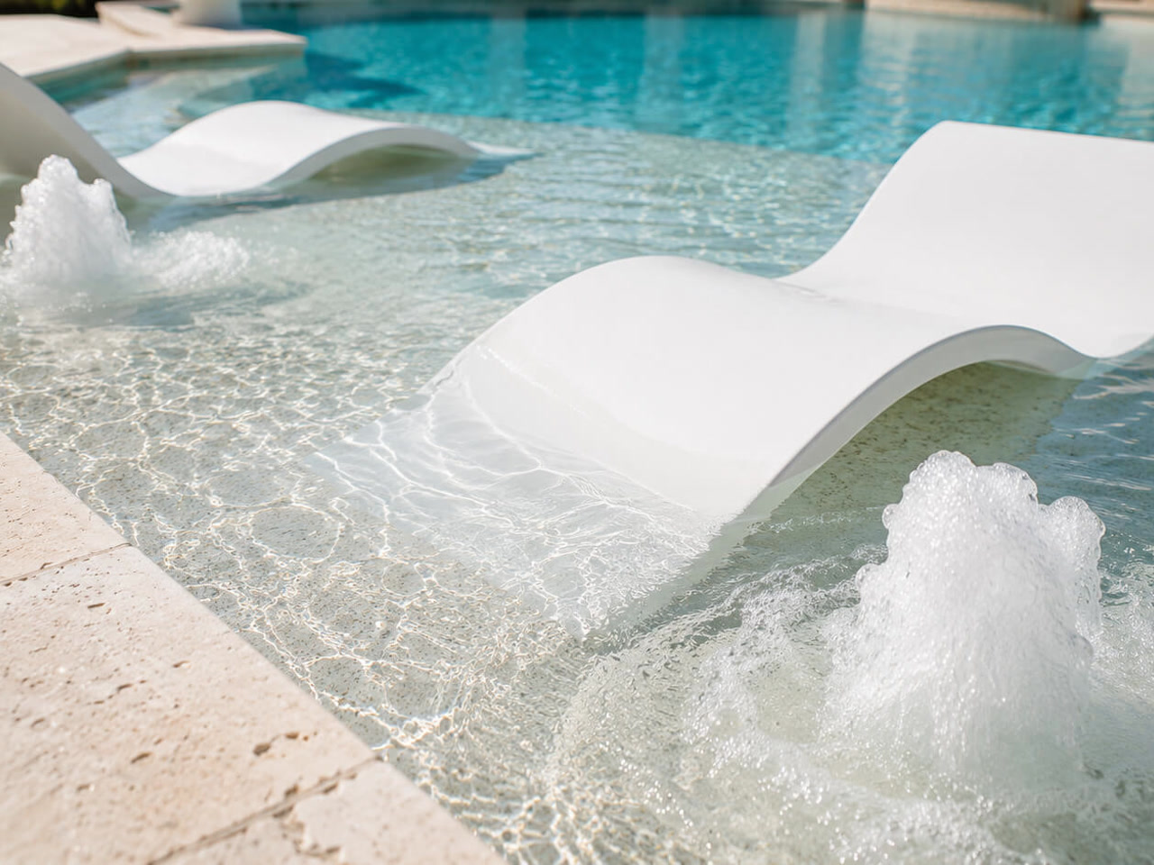 White in water loungers on a shallow sun shelf with bubblers churning on either side at a Pompano Beach residence