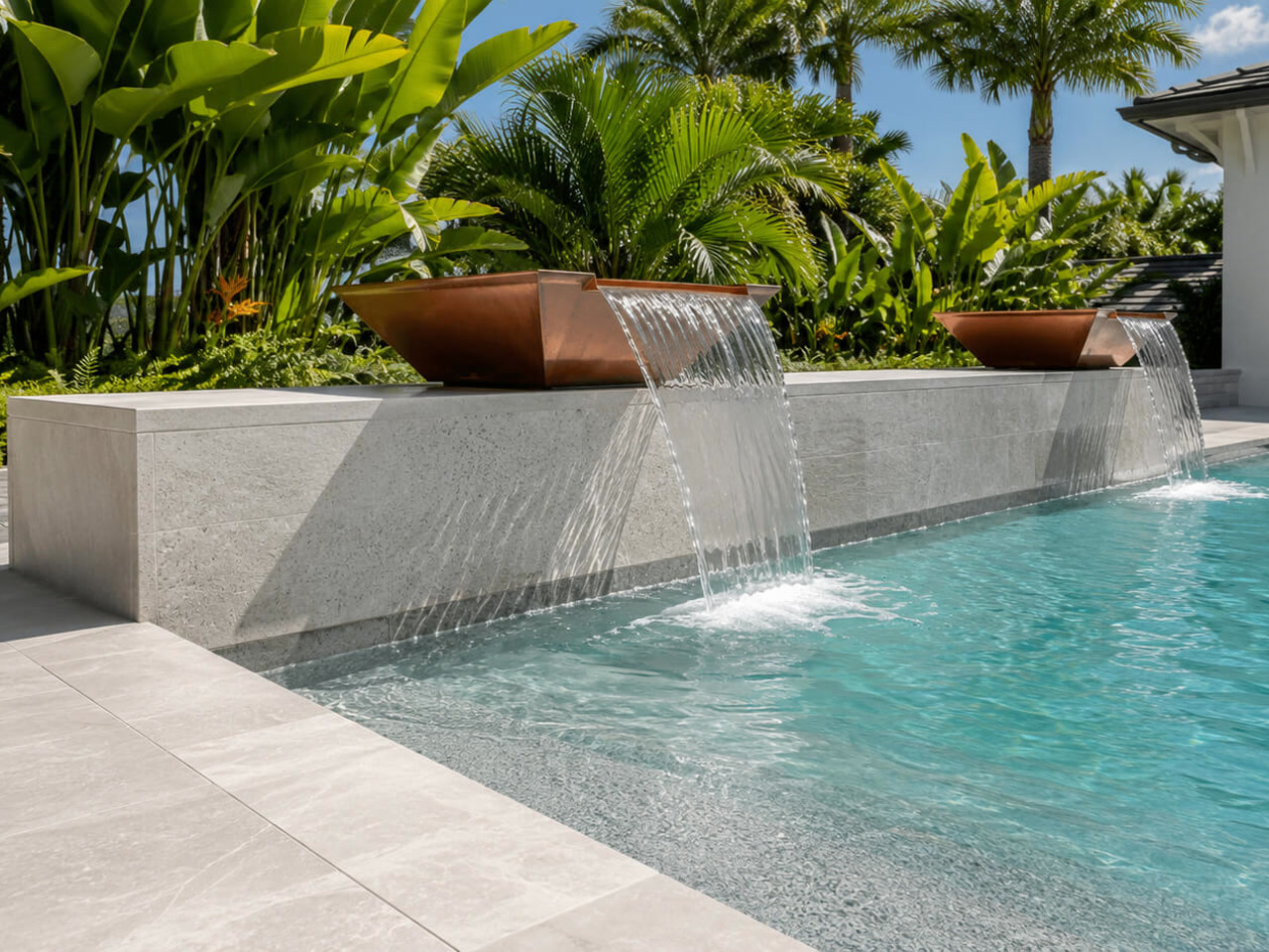 Copper scupper bowls spilling over a light stone wall into a Pompano Beach pool framed by tropical planting