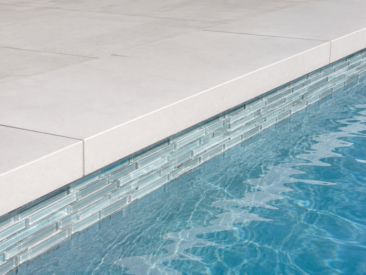 Squared off light stone coping over a band of linear pale blue glass waterline tile in Boca Raton