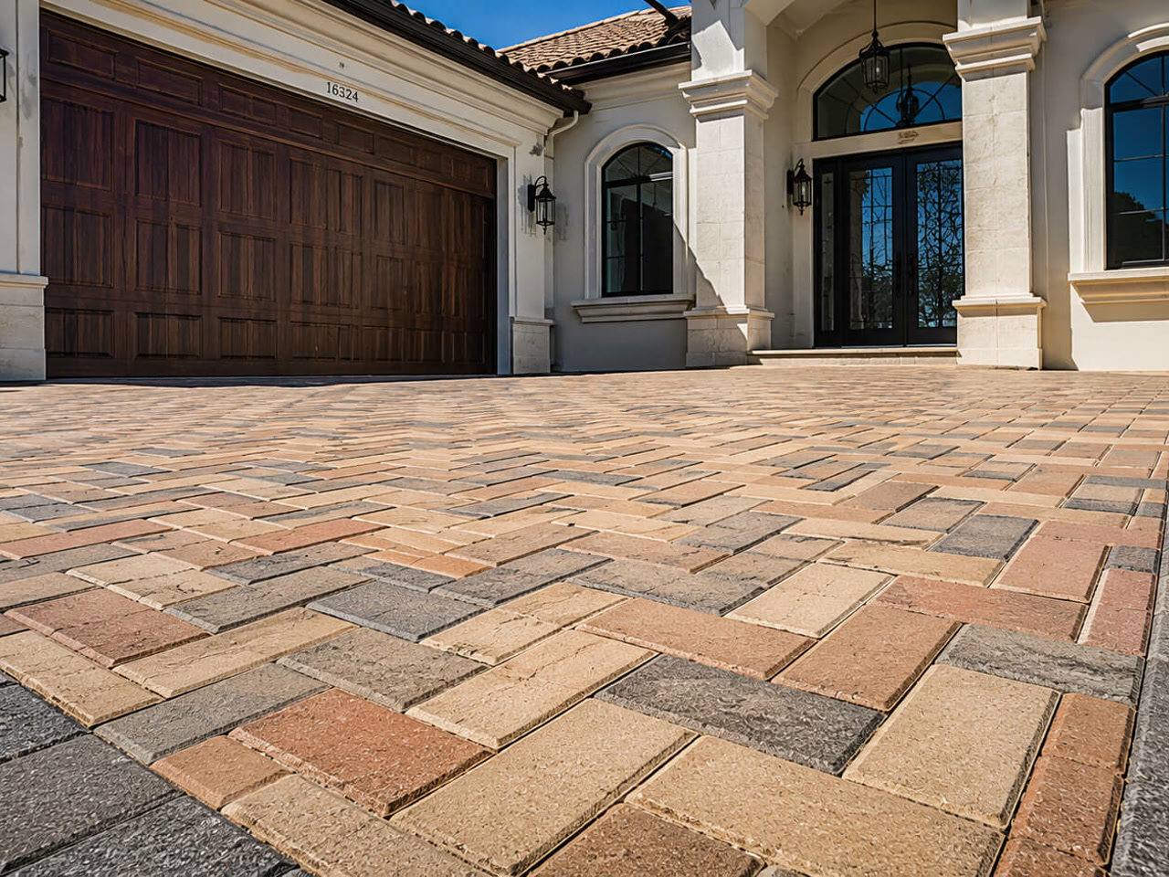 Paver driveway in a blended tan and terracotta herringbone pattern with a charcoal border, leading to a Mediterranean style Florida home