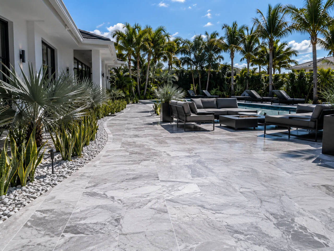 Gray marble paver patio curving along a modern home to a poolside lounge with a fire table