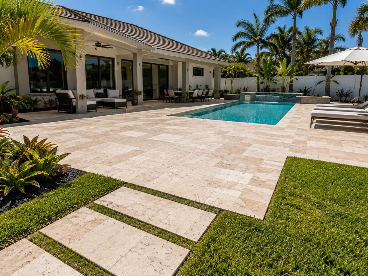Travertine paver patio beside a pool with a stepping stone walkway leading out to the lawn