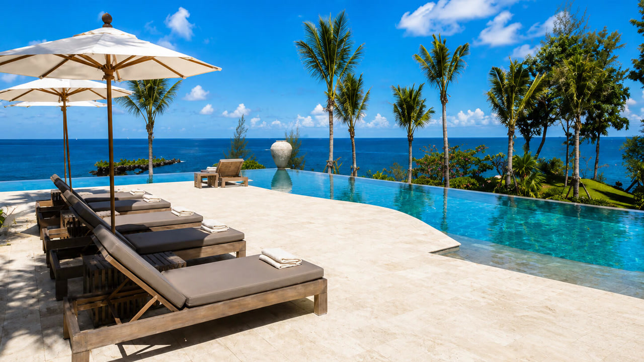Ivory travertine paver pool deck around an infinity pool overlooking the ocean, with loungers and umbrellas