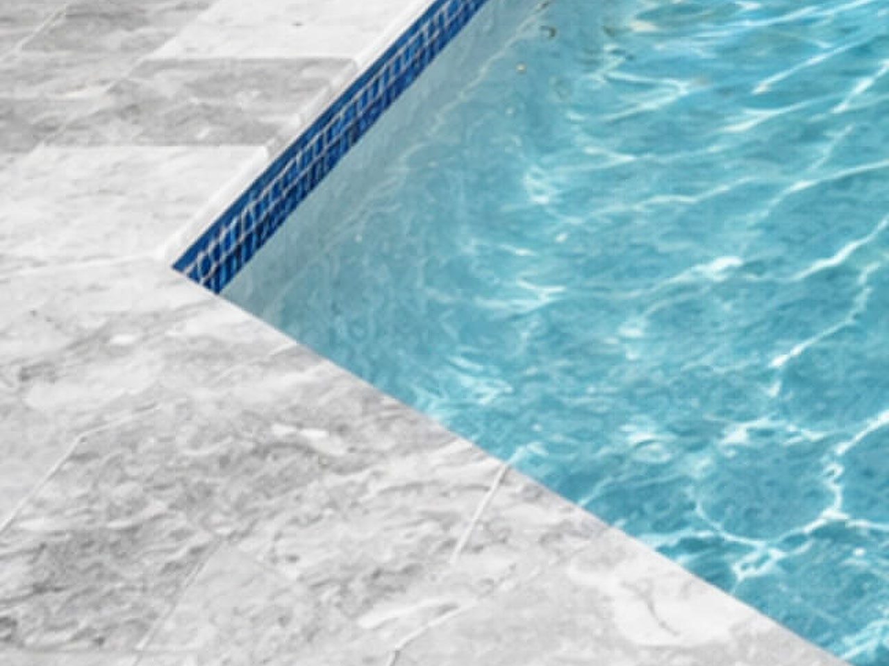 Squared gray marble coping profile meeting the pool corner over a cobalt mosaic waterline band
