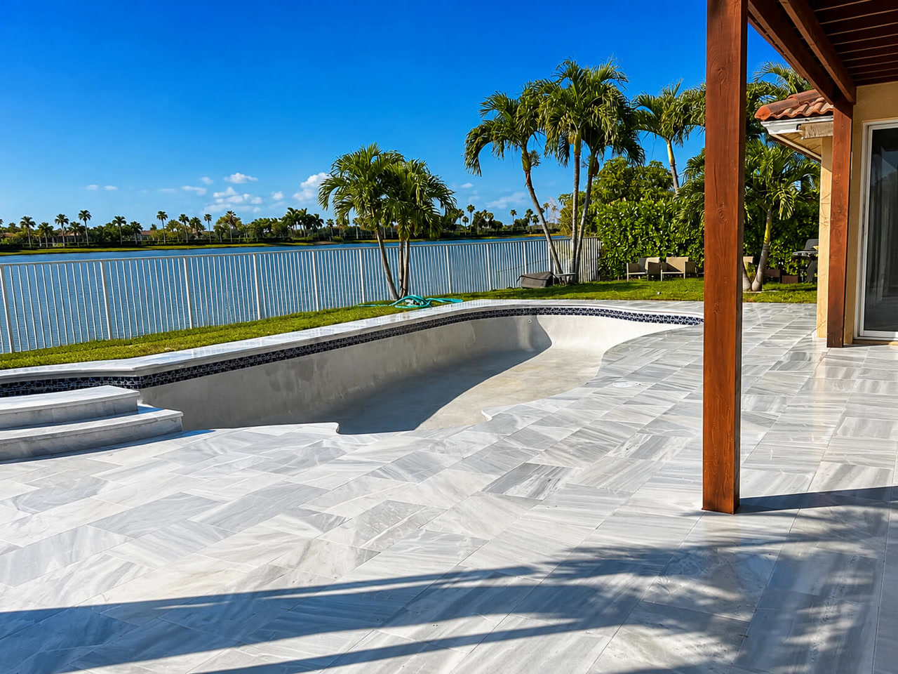 Drained pool shell with fresh gray surface prepared for resurfacing, ringed by a new marble paver deck