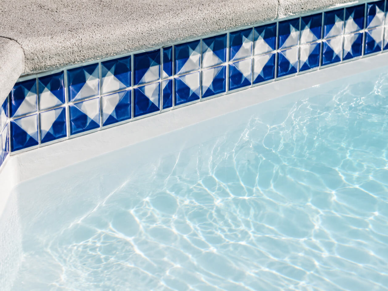 Classic white plaster pool finish under a blue and white patterned tile border and textured concrete coping