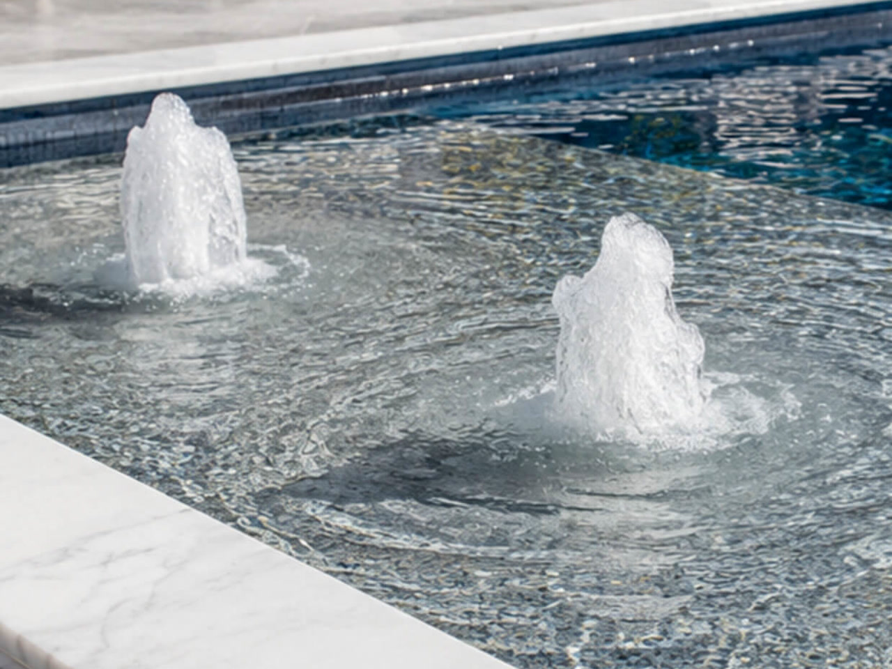 Two bubbler fountains on a mosaic tiled sun shelf edged with white marble coping