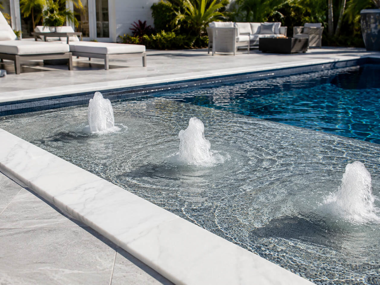 Three bubblers running across a mosaic tiled sun shelf edged in white marble coping