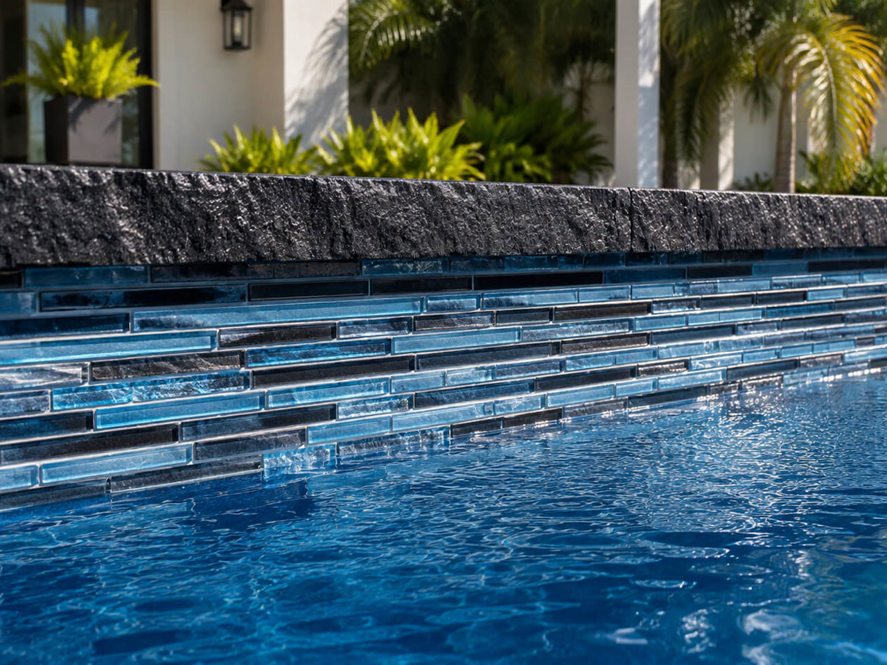 Finished pool edge with a rough cut black stone coping over linear blue glass waterline tile